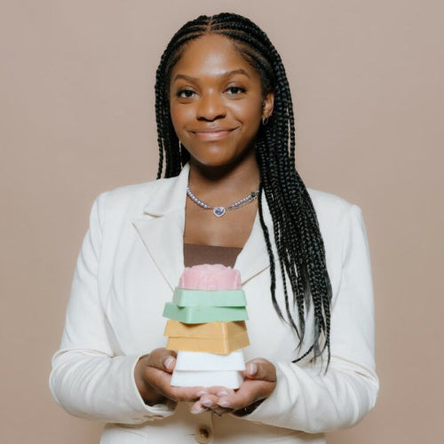 Woman in a white suit holding a stack of colorful boxes against a beige background